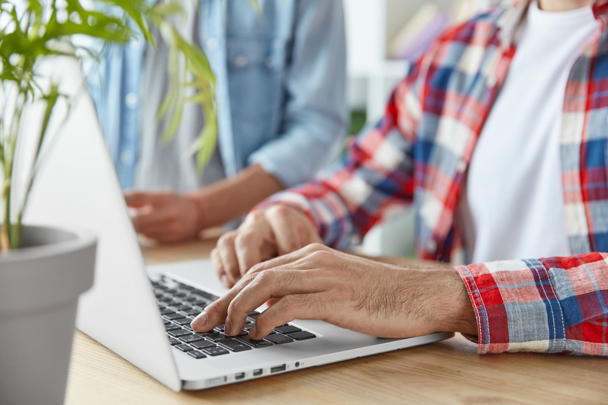 Cropped shot of two male bloggers type publication on laptop computer, use laptop computer, sit at w